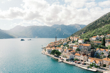 Ancient houses with red roofs on the shore of the Bay of Kotor at the foot of the mountains. Perast, Montenegro. Drone