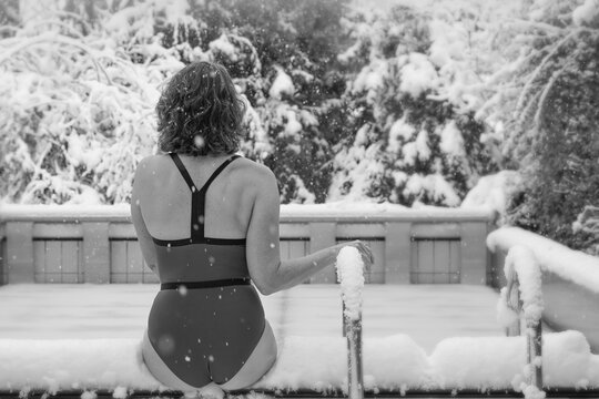 Frau im Schwimmanzug sitzt am Poolrand - der Schnee und Eis statt Wasser anbietet