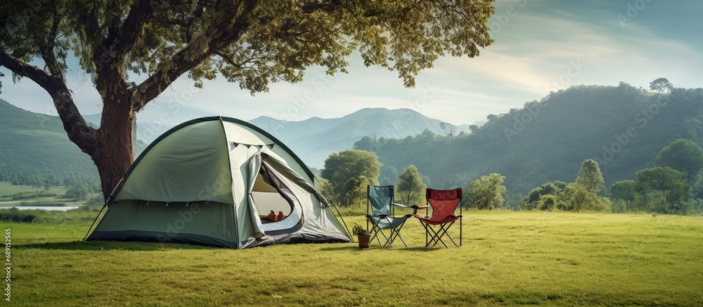Poster campsite with white tent tree green grass mountain backdrop camping gear chairs copy space image pla