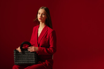 Fashionable confident woman wearing trendy red suit blazer,  holding stylish black tweed bag,...