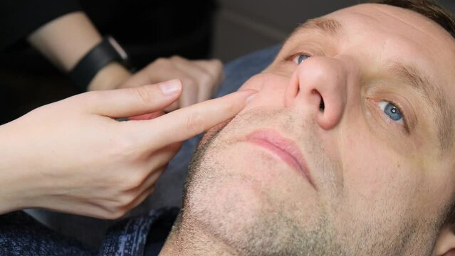 An adult man lies on a couch at a cosmetologist. The hands of a female cosmetologist show how the injection will be given. Close-up.