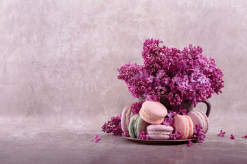 Sweet pastel french macaroons and lilac flowers on gray background. Beautiful composition for bakery and pastry shop with copy space for text