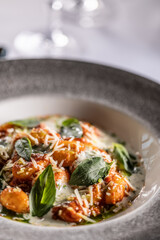 Gnocchi pomodoro with mascarpone, cream, basil and parmesan, in a stylish plate on a restaurant table