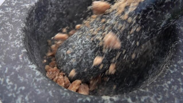 Large pieces of the sweet brown sugar are falling into the grey stone mortar