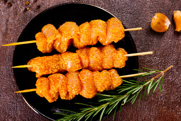 Raw chicken skewers in marinade with spices on a black plate - 689173113