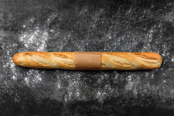 Baguette and wheat flour on black background.