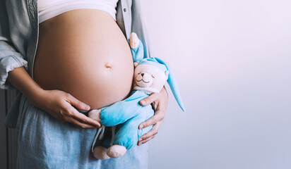 Closeup woman pregnant belly with teddy toy. Concept of pregnancy, maternity, prepare for baby.