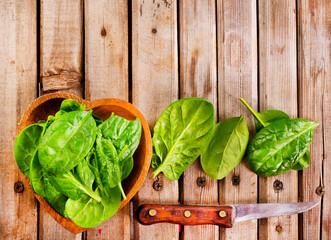 Fototapeta premium Fresh spinach leaves in bowl on rustic wooden table. Top view.