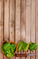 Fresh spinach leaves in bowl on rustic wooden table. Top view.