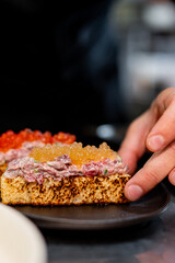 Chef cook hand cooking Canape with brioche, Raw beef meat tartar, salmon red caviar at the restaurant kitchen