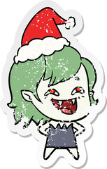 hand drawn distressed sticker cartoon of a laughing vampire girl wearing santa hat