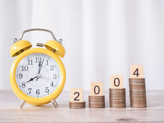 Yellow alarm and Wooden block with number 2024 on stack of coins. The concept of saving money, manage time to success Financial, Investment and Business growing in new year 2024.