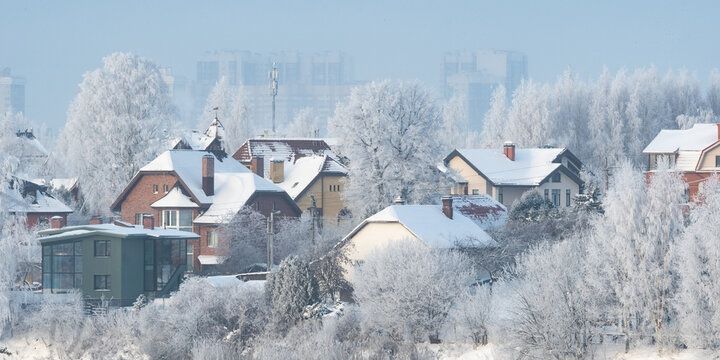 A russian village of private low-rise buildings, covered in snow, with high-rise residential buildings in the distance. Winter village in snow and frost.