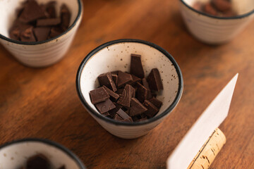Pieces of dark chocolate in white small cup on wooden table