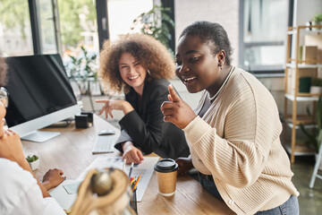 creative team of ambitious multiethnic businesswomen talking near computer and documents in office