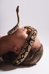 Young woman with a python snake slithering over her face, covering her eyes.