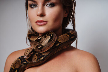 Beautiful woman with python snake elegantly slithering over her neck