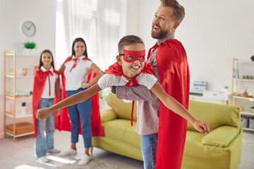 Happy smiling family of four in red super hero costumes playing game imagine flying at home. Young...