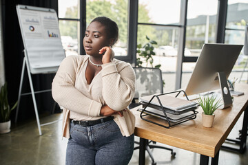 thoughtful african american plus size businesswoman looking away while standing in modern office