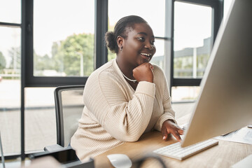 satisfied african american plus size businesswoman looking on computer monitor in office, success