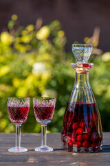 Homemade red cherry brandy in glasses and in a bottle on a wooden table in a summer garden