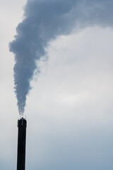High chimney with pillar of smoke against grey sky