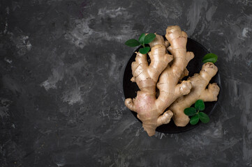 Raw ginger root on a black plate on a dark background. Horizontal, free space for printing.