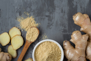 Whole raw root and sliced ​​ginger, ceramic bowl with ginger spice and green leaves on a dark...