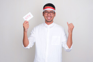 Indonesian man smiling and showing his little finger while holding election vote paper