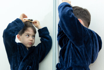 cute adorable preschooler kid boy brushing hair in front of double sided mirror or isolated on...