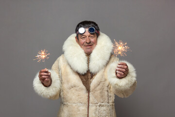 A mature man in a warm fur coat with a white fox collar holds a Christmas firework, a sparkler, in each hand.