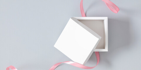 Open white square box mockup with pink ribbon on gray background. Flat lay, top view, copy space