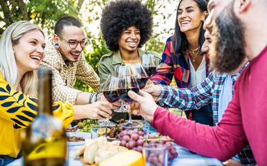 Happy friends drinking red wine at farm house restaurant garden - Millennial people enjoying lunch break together outside - Hands holding wineglasses at sunset golden hour