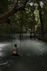 Woman sitting on a swing on a river or lake among the trees