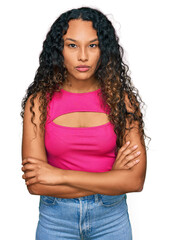 Young hispanic woman with curly hair wearing pink top skeptic and nervous, disapproving expression on face with crossed arms. negative person.