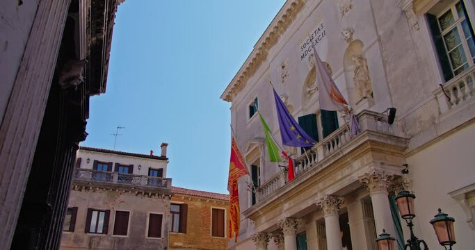 Historic white building of the Teatro La Fenice, theatre in Venice, with Italian and European flags, and architectural details in a European city.