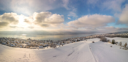 Winter magic on Lake Zurich, snow-covered idyll, clear air at golden hour over picturesque houses and trees, panoramic view from the air, Erlenbach in winter, panorama with the drone, travel location