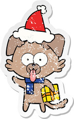 Naklejka premium hand drawn distressed sticker cartoon of a dog with christmas present wearing santa hat