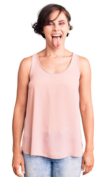 Beautiful young woman with short hair wearing casual style with sleeveless shirt sticking tongue out happy with funny expression. emotion concept.