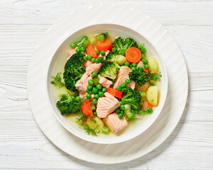 salmon, veggies and green herbs soup in bowl
