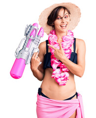 Beautiful young woman with short hair wearing bikini and hawaiian lei holding water gun smiling...