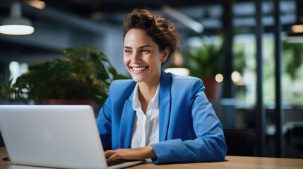 A smiling businesswoman works on a laptop in a modern office