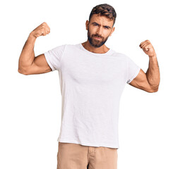 Young hispanic man wearing casual white tshirt showing arms muscles smiling proud. fitness concept.