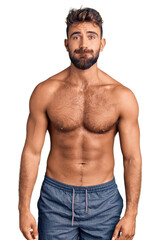 Fototapeta premium Young hispanic man wearing swimwear shirtless puffing cheeks with funny face. mouth inflated with air, crazy expression.