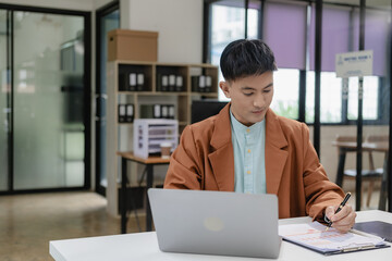 Fototapeta premium Businessman, manager, CEO, handsome Asian man, middle aged man sitting in office, working on paperwork, checking and reading documents, contracts and accounting reports with laptop.
