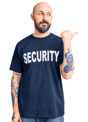 Young handsome man wearing security t shirt smiling with happy face looking and pointing to the side with thumb up.