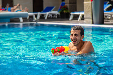 A man plays with a water pistol in the pool. Selective focus.