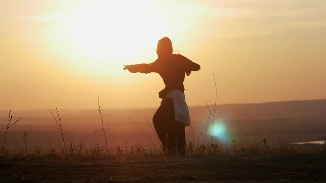 A girl dancing on a hill, against the background of the sun. Moving shot