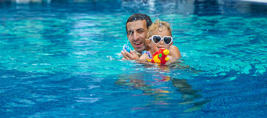 A child and his father play with a water pistol in the water. Selective focus.