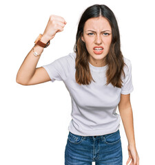 Young beautiful woman wearing casual white t shirt angry and mad raising fist frustrated and...